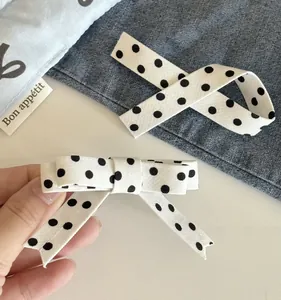 Detailed view of white fabric hair clip with black polka dots and soft ribbon texture