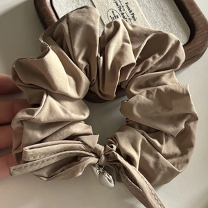 Beige satin scrunchie with large bow and silver heart pendant on wooden tray