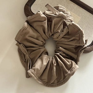 Detail view of khaki satin scrunchie with small ribbon bows on a linen tray