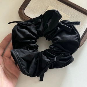 Close-up of black matte satin scrunchie featuring elegant ribbon detailing and soft folds