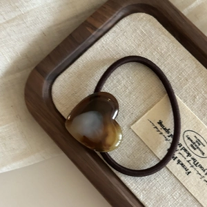 Vue détaillée d'un élastique coeur en résine écaillée sur un plateau en bois et lin