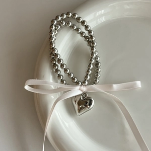 Vue détaillée du bracelet à perles argentées avec pendentif cœur poli et nœud rose