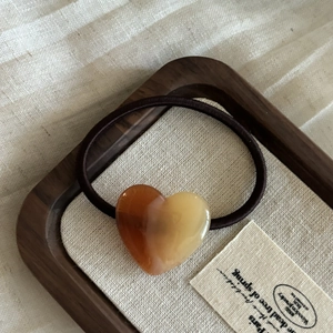 Détail du pendentif cœur en résine marron sur élastique à cheveux dans un plateau en bois