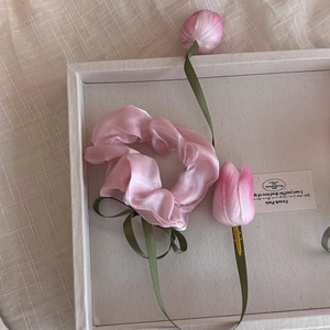 Détail d'un chouchou en organza rose avec nœud en ruban vert foncé et décor floral