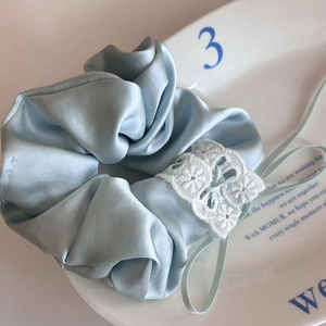 Light blue satin hair scrunchie with white lace trim on a decorative ceramic plate