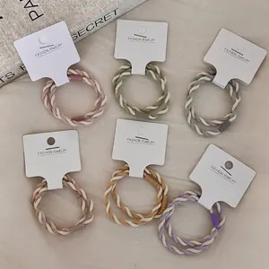 Set of 6 elastic braided hair ties in cream colors on a beige fabric background