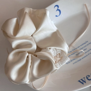 Creamy satin hair scrunchie with white lace trim and ribbon bow on a decorative tray