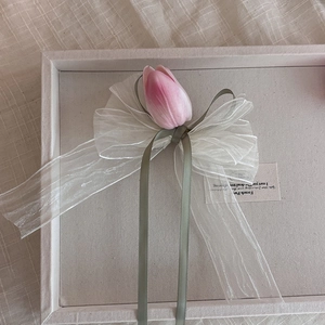 Détail d'un nœud en organza blanc avec tulipe rose et rubans verts sur un plateau