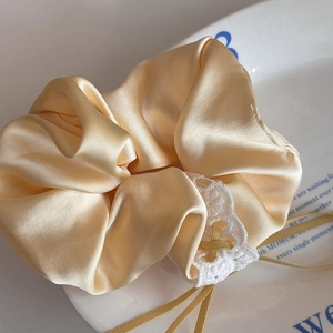 Close-up of champagne satin scrunchie with white lace trim and delicate ribbons on a plate