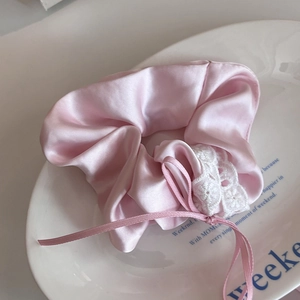 Detail of pink satin scrunchie with white lace trim and delicate ribbon bow on a tray