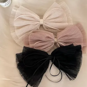 Close-up of three layered mesh bow hair clips in cream, pink and black colors