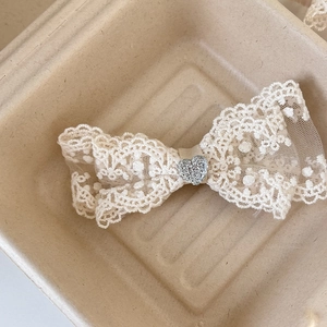 Dettaglio di un fiocco in pizzo bianco con un cuore scintillante come accessorio capelli
