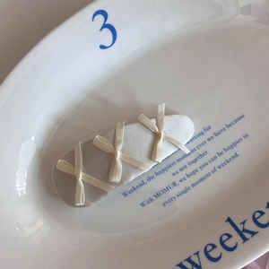 Detailed view of cream satin hair clip with three delicate ribbon bows on white ceramic plate
