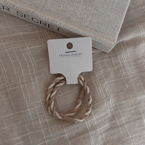 Detailed view of high-elasticity braided hair ties in cream and pink on a display card