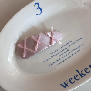 Close-up of a pink satin hair clip with three delicate ribbon bows on a ceramic plate