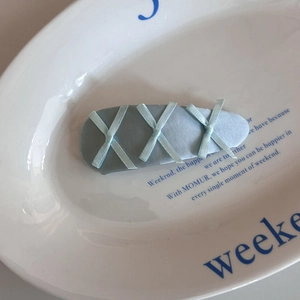 Detailed view of light blue fabric hair clip with criss-cross ribbon accents on a white plate