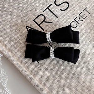 Detail of pair of black satin bow hair clips with white faux pearls on linen background