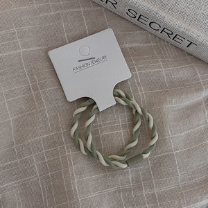 Close-up of sage green and cream braided elastic hair ties on a fashion jewelry display card