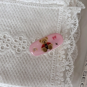 Dettaglio molletta rosa ovale con orsetto e fiocco su pizzo bianco decorativo