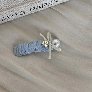 Detail of blue tulle hair clip with ribbon bow, white pearl, and gold engraved charm