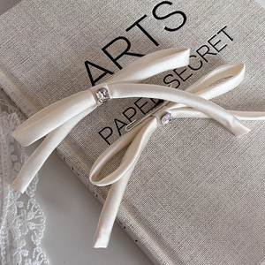 Close-up of cream satin bow hair clip with square crystal center and elegant long ribbons