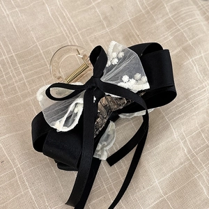 Détail d'une pince à cheveux avec nœud en satin noir et broderie en dentelle blanche