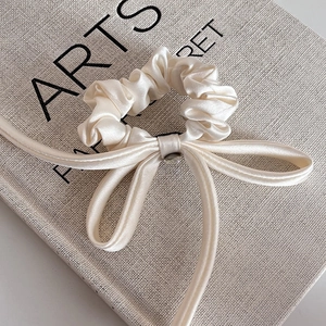 Elegant cream satin hair scrunchie with long ribbon bow on a textured art book base