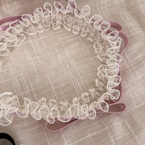 Détail d'un serre-tête en dentelle beige et ruban rose aux bords volantés