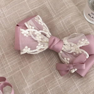 Détail d'une barrette à nœud en satin rose et dentelle florale brodée sur du lin