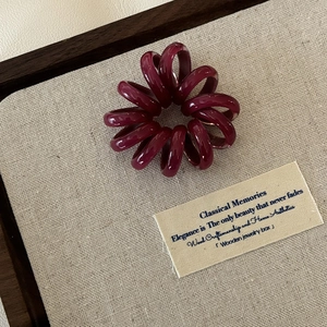 Eleganter weinroter Spiral-Haargummi auf einer Vintage-Leinwand für feines Styling