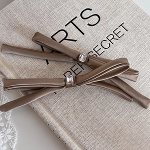 Pair of brown satin bow hair clips with emerald-cut crystals on a linen book background