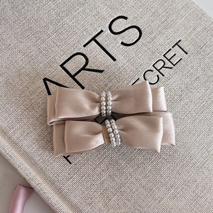Detail of satin bow hair clips in champagne color featuring double row pearl centers