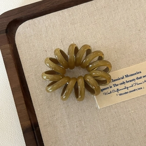 Olivgrünes spiralförmiges Telefonkabel-Haargummi auf einem Holztablett im minimalistischen Stil