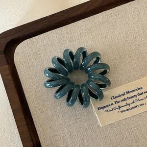 Detailansicht eines flexiblen Spiral-Haargummis in Dunkelgrün auf einem Display-Tablett