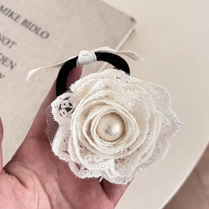 Macro detail of a 3D white lace rose hair tie with a central pearl on a black elastic band