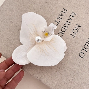 Detail showing white orchid flower hair clip with a center pearl and delicate petal texture