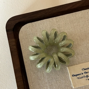 Makro-Detail eines hellgrünen, transparenten Spiralhaargummis auf einem Holztablett