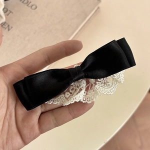 Detailed macro view of black satin bow hair clip with intricate white lace floral edges