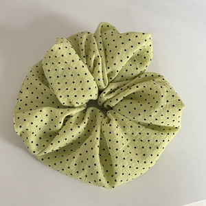 Détail d'un chouchou vert clair à pois noirs avec une texture de tissu ondulé fin