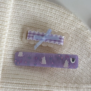 Details von lila Blumen-Haarklammern mit Schleifen und Katzenmotiven auf Strickstoff