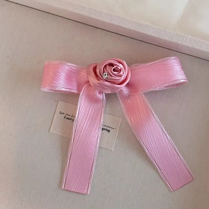 Detalle de horquilla con lazo de satén rosa, rosa delicada y centro de pedrería