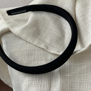 Macro detail of black satin headband with handmade label on a textured linen background