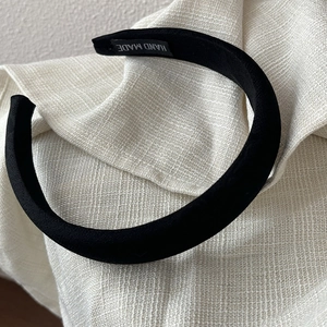 Detailed close-up of textured black satin headband with handmade label on a beige fabric surface