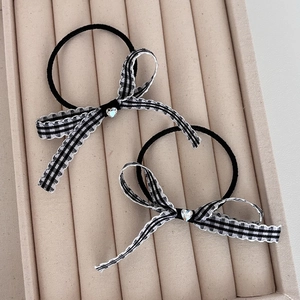 Detail view of two checkered bow hair ties with crystal hearts on a beige velvet tray
