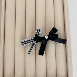 Detailed close-up of a black satin and plaid bow hair clip with a crystal heart center