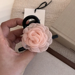 Details einer schwarzen Kamelien-Haarklammer mit rosa Satinblüten und Netzstruktur
