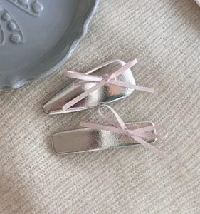 Détail de barrettes en cuir argenté avec nœuds en ruban rose sur tricot blanc doux