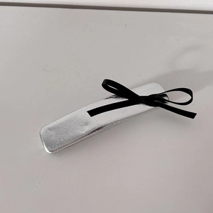 Détail de la barrette en métal argenté avec surface texturée et petit nœud en ruban noir
