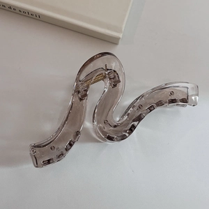 Detailed close-up of translucent grey wave hair claw with metal spring on minimalist background