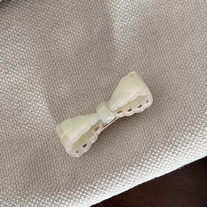 Detail of cream acetate bow hair clip with decorative hollowed-out scalloped edges